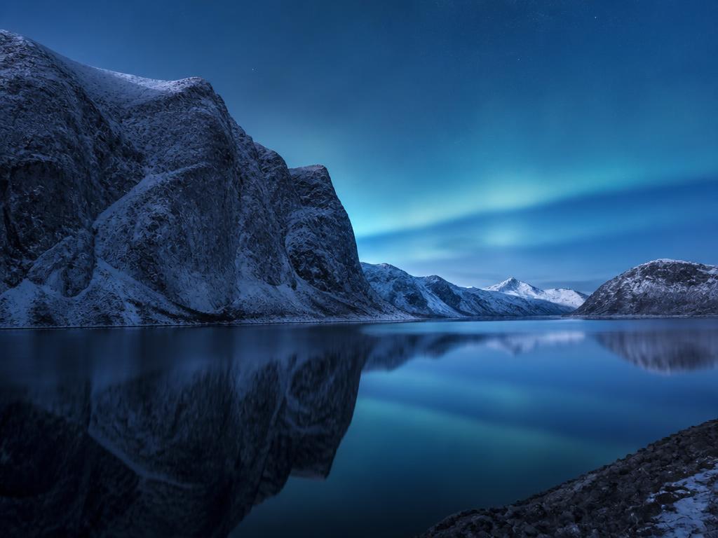 Snow-dusted Norwegian fjord glowing under the northern lights for the Norway Collection